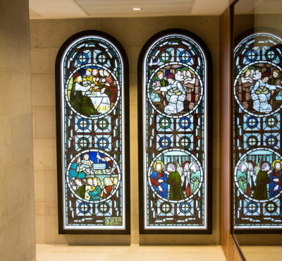 The windows designed by Burne-Jones and executed by Morris at Cohen Quad, with a reflection in the window of the Neil Blair Special Collections Reading Room