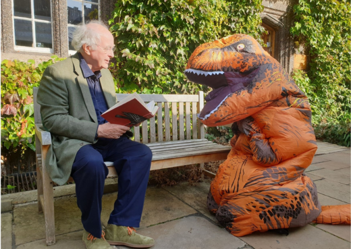 Alumnus Sir Philip Pullman Pictured reading his a novel to Exeter's Giving Day mascot TRexeter in the Front Quad on a bench