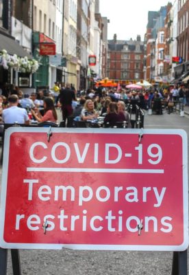 Sign that reads "COVID-19 Temporary Restrictions" on a street filled with people