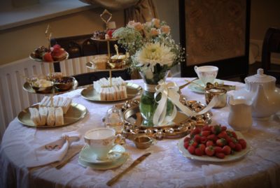 A table set for afternoon tea with tiered trays of sandwiches and pastries, fine china, fresh flowers, and a plate of strawberries.
