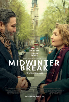 Film poster for Midwinter Break. A man and a woman (both middle-aged) face each other in profile on either side of the image, standing by a canal lined with trees and buildings. The scene is split down the middle, subtly separating them. Both wear winter coats and scarves, suggesting a cool, muted atmosphere. Centered text reads the actors’ names (Lesley Manville and Ciarán Hinds) and the title Midwinter Break, with the tagline: “A day they can’t forget. A truth they can’t escape.” At the bottom: “In cinemas March 20.”